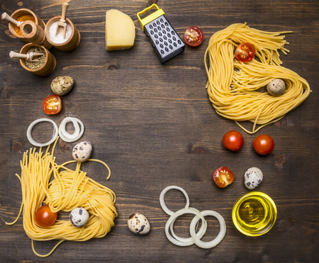 ingredients for cooking vegetarian pasta with cherry tomatoes, onions, parmesan cheese, a variety of spices on rustic wooden background, lined frame with space for textの写真素材
