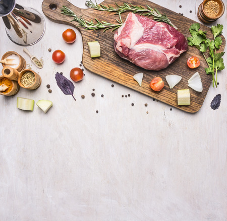 raw pork steak on a cutting board with a vintage cherry tomatoes, candied fruit, cherry tomato, basil, rosemary and other herbs, laid out on a white rustic wooden background, Border, place for textの写真素材