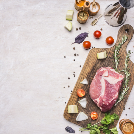 raw pork steak on a cutting board with a vintage cherry tomatoes, candied fruit, cherry tomato, basil, rosemary and other herbs, laid out on a white rustic wooden background, Border, place for textの写真素材