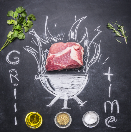 raw pork steak on a chalkboard painted with a burning grill with herbs and spices, butter and inscriptionの写真素材