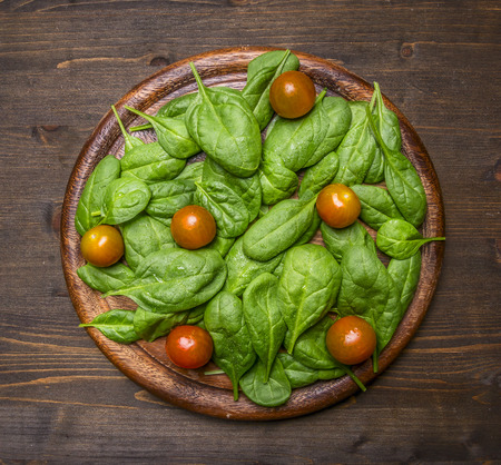 Detox and diet food concept Fresh spinach on a cutting board with cherry tomatoes on a rustic wooden backgroundの写真素材