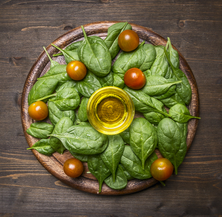 Healthy foods, cooking and vegetarian concept ingredients for the salad, fresh spinach leaves, cherry tomatoes, oil, laid out on a wooden cutting boardの写真素材