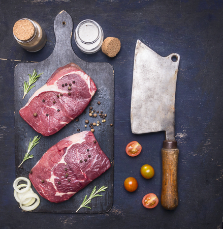 concept of cooking meat, raw ribeye, steak on a cutting board with rosemary, spices, oil and vegetables, with a meat cleaver vintage, Border, place for textの写真素材