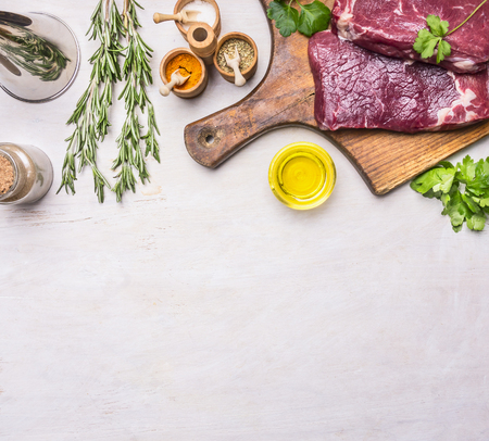 concept of cooking meat, raw ribeye steak on a cutting board with rosemary, spices, oil and vegetables, with a meat cleaver vintage, Border, place for text on a rustic wooden backgroundの写真素材