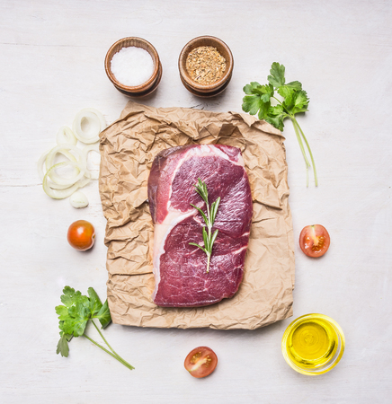 appetizing beef steak on a paper packaging with herbs, cherry tomatoes, seasonings and butter, top view, on a rustic wooden backgroundの写真素材