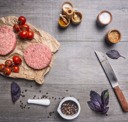 raw cutlet for burgers, with cherry tomatoes and herbs on a packaging paper with unground black pepper, knife for meat on wooden rustic background top view close up place for text,frameの写真素材