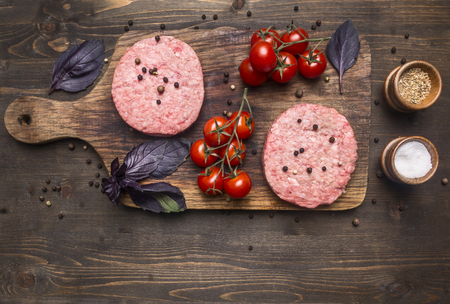 raw cutlet for burgers, with cherry tomatoes and herbs on a cutting board, boarder, space for text on wooden rustic background top viewの写真素材
