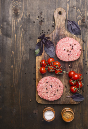 raw cutlet for burgers, with cherry tomatoes and herbs on a cutting board, boarder, space for text on wooden rustic background top viewの写真素材
