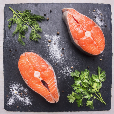 helpful sports foods, cooking two fresh salmon steak with herbs and spices,on a cutting board stone, top view close upの写真素材
