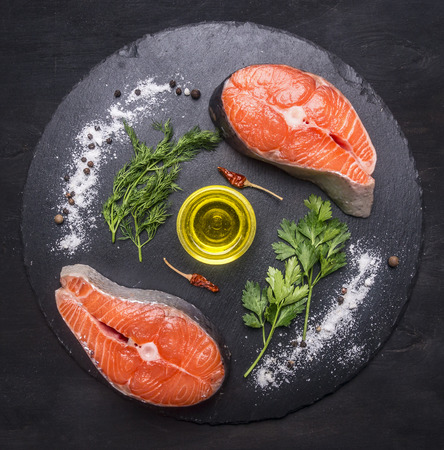 two raw salmon steak on a stone cutting board with salt, pepper, herbs, butter and lined all around, top viewの写真素材