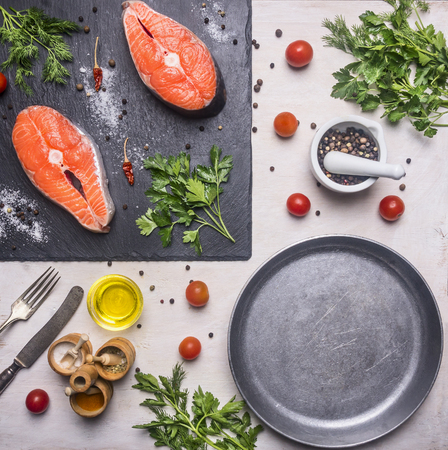 Healthy foods, cooking and sport concept Two fresh salmon steak with herbs and spices on a cutting board stone, laid near cherry tomatoes, whole pepper, pan frying, oil, top viewの写真素材