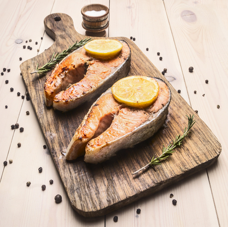 appetizing fried salmon steak on a cutting board with lemon and rosemary and pepper unground close upの写真素材