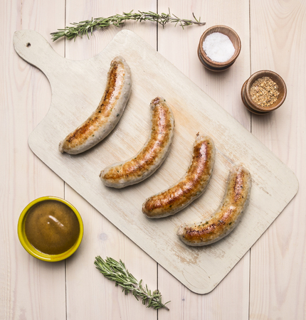 grilled sausages lying on vintage cutting board with rosemary, spices, curry sauce and meat fork on a rustic background top viewの写真素材