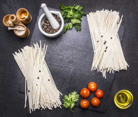 noodles with tomatoes and oranges on a cutting board with herbs, frame space for textの写真素材