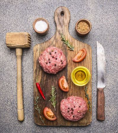 ingredients for cooking burgers, ground beef, tomatoes, red pepper and other spices laid out on a cutting board with a knife and a hammer  for meatの写真素材