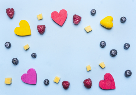 blueberry raspberry and mango, decorative hearts lined frame on a blue background, space for textの写真素材