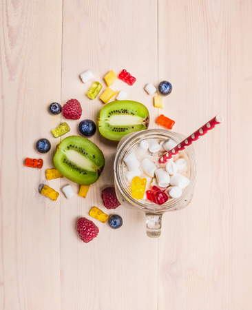 fresh fruit smoothies with berries, marshmallows, kiwi and jelly in bank with a pen on a white background wooden top view close upの写真素材