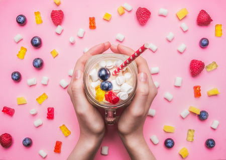 girl holding a fresh smoothie with raspberry, kiwi and bananas on a pink background, with the expansion around the multicolored hearts, berries, jelly and marshmallow healthy food, valentines dayの写真素材