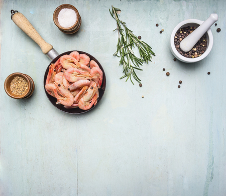 Asian cooking ingredients with fresh small shrimp in a small frying pan, herbs and pepper on wood blue background top view border, place for textの写真素材