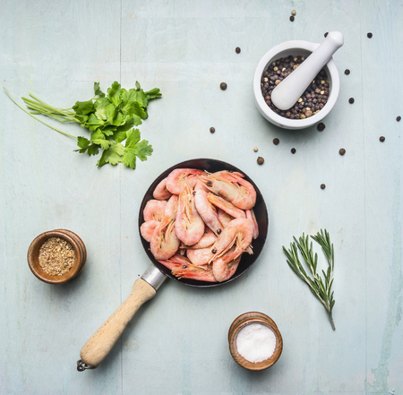 Asian cooking ingredients with fresh small shrimp in a small frying pan, herbs and pepper on wood blue background top viewの写真素材