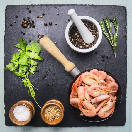 Asian cooking ingredients with fresh small shrimp in a small frying pan, herbs and pepper on stone black backgroundの写真素材