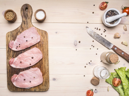 Ingredients for cooking Succulent Pork steak on vintage cutting board with a variety of vegetables and herbs on a white wooden background, with space for textの写真素材