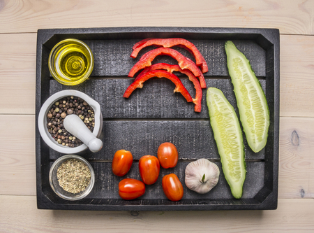 Ingredients for cooking vegetarian salad with herbs and butter laid out in a wooden tray cucumbers, peppers, cherry tomatoes and garlicの写真素材