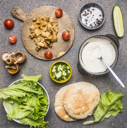 Ingredients for cooking homemade shawarma, fried chicken with seasonings, pita, sliced ??cucumbers, seasonings and spices, sauce with garlic, boarder, place for textの写真素材