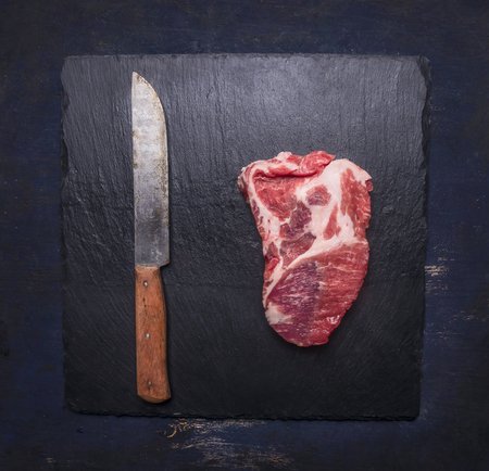 Appetizing juicy raw pork steak on a black cutting board with a meat knife top viewの写真素材