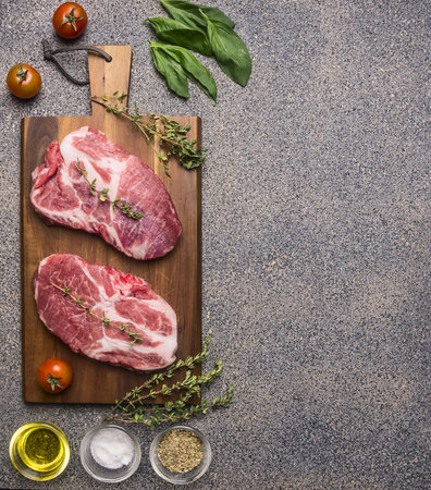 Ingredients for cooking Two fresh raw pork steaks with seasonings and herbs, cherry tomatoes and butter, lined on a cutting board top view borderの写真素材