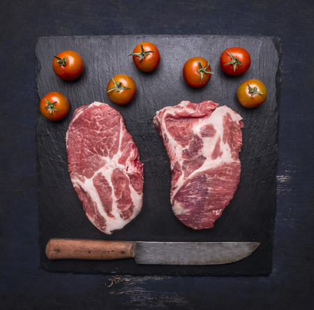 Two fresh raw pork steaks with cherry tomatoes and seasonings, knife, food for athletes, protein and fiber, on a cutting board, top viewの写真素材