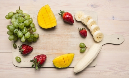Fresh organic Smoothie ingredients Bananas, mangoes, strawberries and grapes, lined with a frame on a cutting board, space for textの写真素材