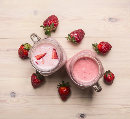 Red smoothies made of strawberries and milk, in a stylish jar, a row of berries are laid out, on a white wooden backgroundの写真素材
