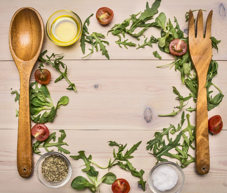 Wooden fork and spoon, arugula and other ingredients for cooking fresh healthy salad lined with a frame on a white wooden table space for textの写真素材