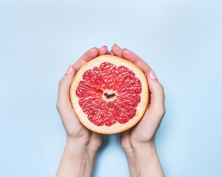 Appetizing ripe large grapefruit in the hands of a girl, on a blue background, space for textの写真素材
