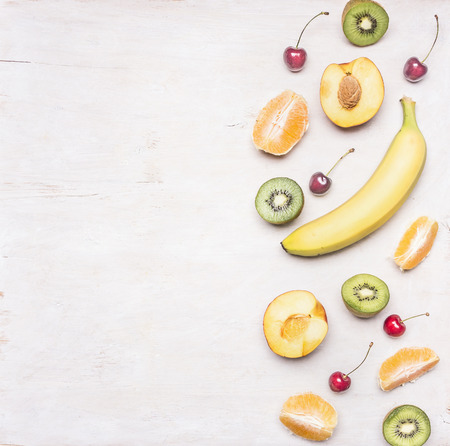 Ingredients for fruit salad, kiwi, peaches, oranges, cherries, bananas, on a white wooden rustic background, border Space for textの写真素材