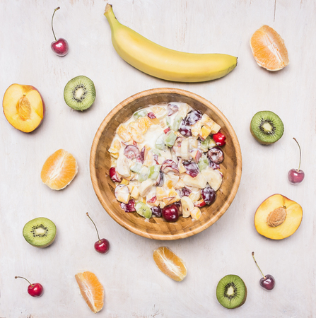 Ingredients for fruit salad, kiwi, peaches, oranges, cherries, bananas, in a wooden bowl on a white wooden rustic backgroundの写真素材