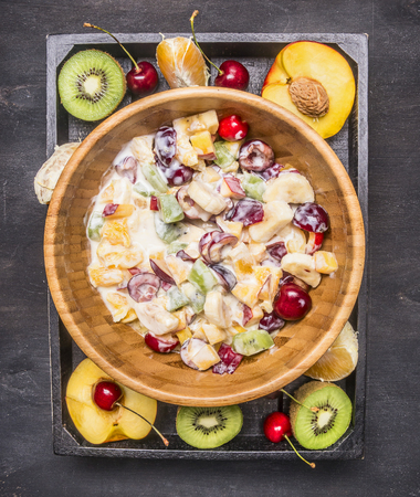 Preparation of fruit salad in a wooden bowl, around lie ingredients, kiwi, cherry, peaches and oranges, top viewの写真素材