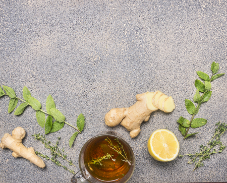 Aromatic hot tea with ginger, lemon balm and thyme with lemon, in a glass mug, on a granite rustic background border space for textの写真素材