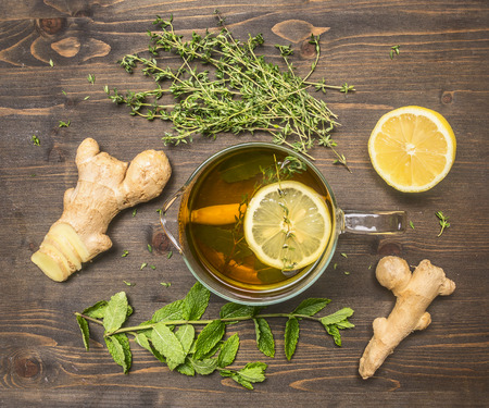 Cooking concept Hot aromatic tea with a root of ginger, thyme, lemon, melissa on a wooden rustic backgroundの写真素材