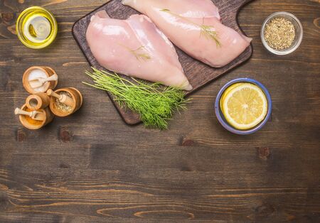 Preparation of chicken breast with dill and lemon and seasonings, cutting board, knife for meat, on a wooden rustic background, Space for text, borderの写真素材