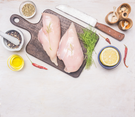 Preparation of chicken breast with dill and lemon and seasonings, cutting board, knife for meat, on a wooden rustic background, Space for text, borderの写真素材