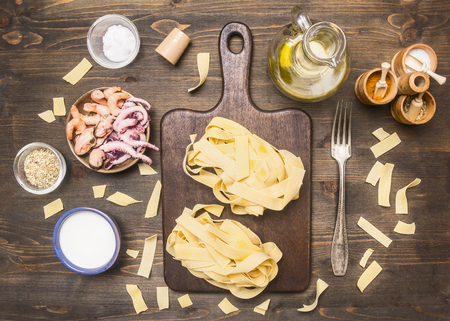 Concept of cooking pasta with seafood, octopus, squid, mussels, shrimps, tomatoes, peppers, various seasonings lined around the cutting board on rustic wooden backgroundの写真素材