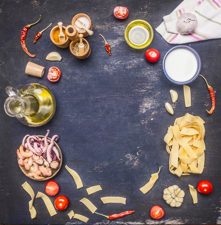 Concept of cooking pasta with seafood, octopus, squid, mussels, shrimps, tomatoes, peppers, various condiments on rustic wooden background, space for text frameの写真素材