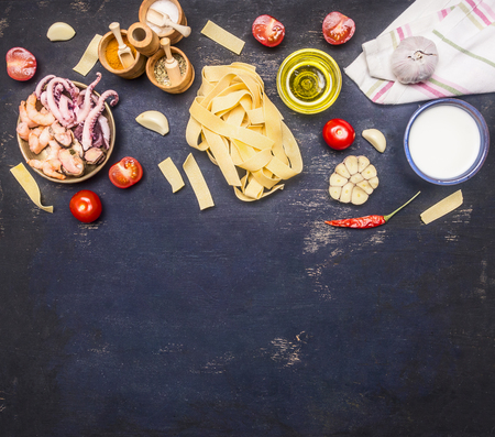 Concept of cooking pasta with seafood, octopus, squid, mussels, shrimps, tomatoes, peppers, various condiments on rustic wooden background, space for text borderの写真素材
