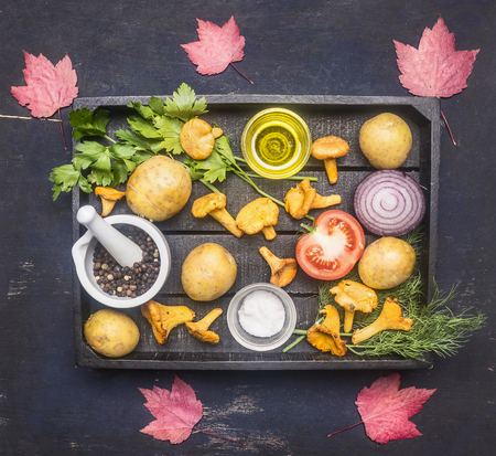 fresh raw chanterelles with potatoes, herbs, seasonings, onions, tomatoes, oil and autumn leaves, in a wooden box, on a rustic background, top viewの写真素材