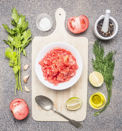 Ingredients for the preparation of cold tomato soup, sliced ââtomatoes, greens, oil, garlic, black pepper, On a white cutting board, on a rustic granite backgroundの写真素材