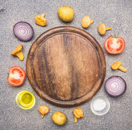 fresh raw chanterelles with potatoes, herbs, seasonings, onions, tomatoes, oil lined around the cutting board, place for text, on rustic background, top viewの写真素材