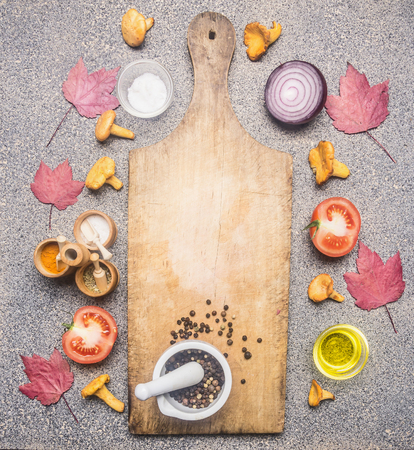 concept of cooking autumn mushrooms, chanterelles, lined around a cutting board, with seasonings, onions, vegetables and maple leaves, on a granite rustic background, top view, space for textの写真素材