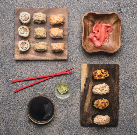 variety of rolls on a wooden plate with soy sauce and ginger, wasabi beside lie red chopsticks, on rustic background, top viewの写真素材